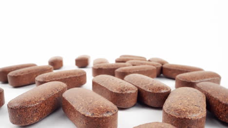 array of brown herbal supplement tablets scattered on white surface