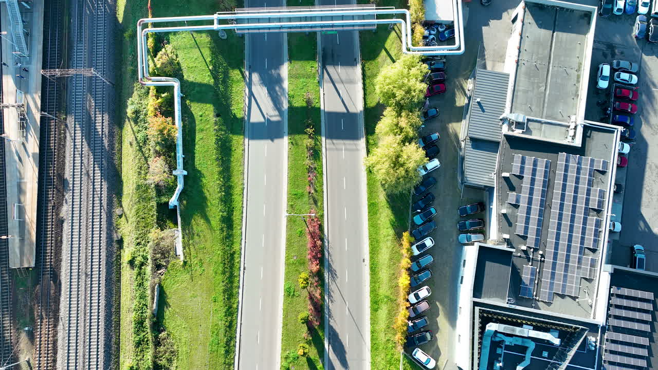 Top view of dual-lane road near railway tracks and solar rooftops in bright daylight