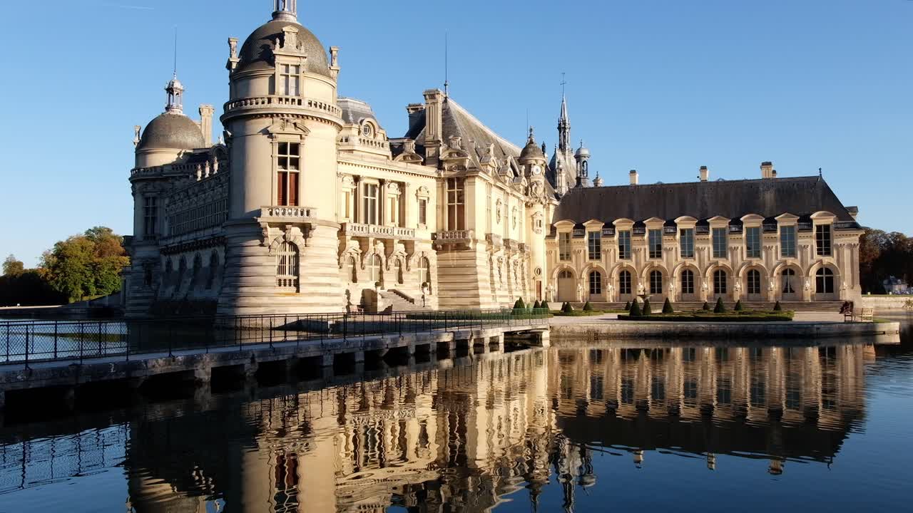 View of the Chateau de Chantilly castle surrounded by immense mirrors of water in Chantilly, Oise, France in daylight