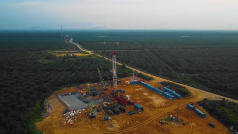 Cinematic-Drone-Footage-of-Onshore-Drilling-Rig-equipment-structure-for-oil-exploration-and-exploitation-in-the-middle-of-jungle-surrounded-by-palm-oil-trees-during-sunset-and-high-oil-price