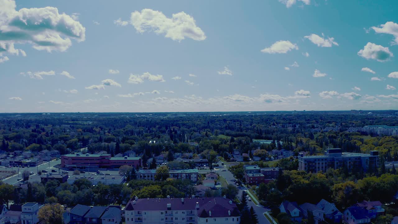 aerial flyover busy suburb town of low rise buildings both residential and commercial on a hot sun pulsing elcipse of summer day with cumulis clouds a gradations of blue skys and a steady fast traffic