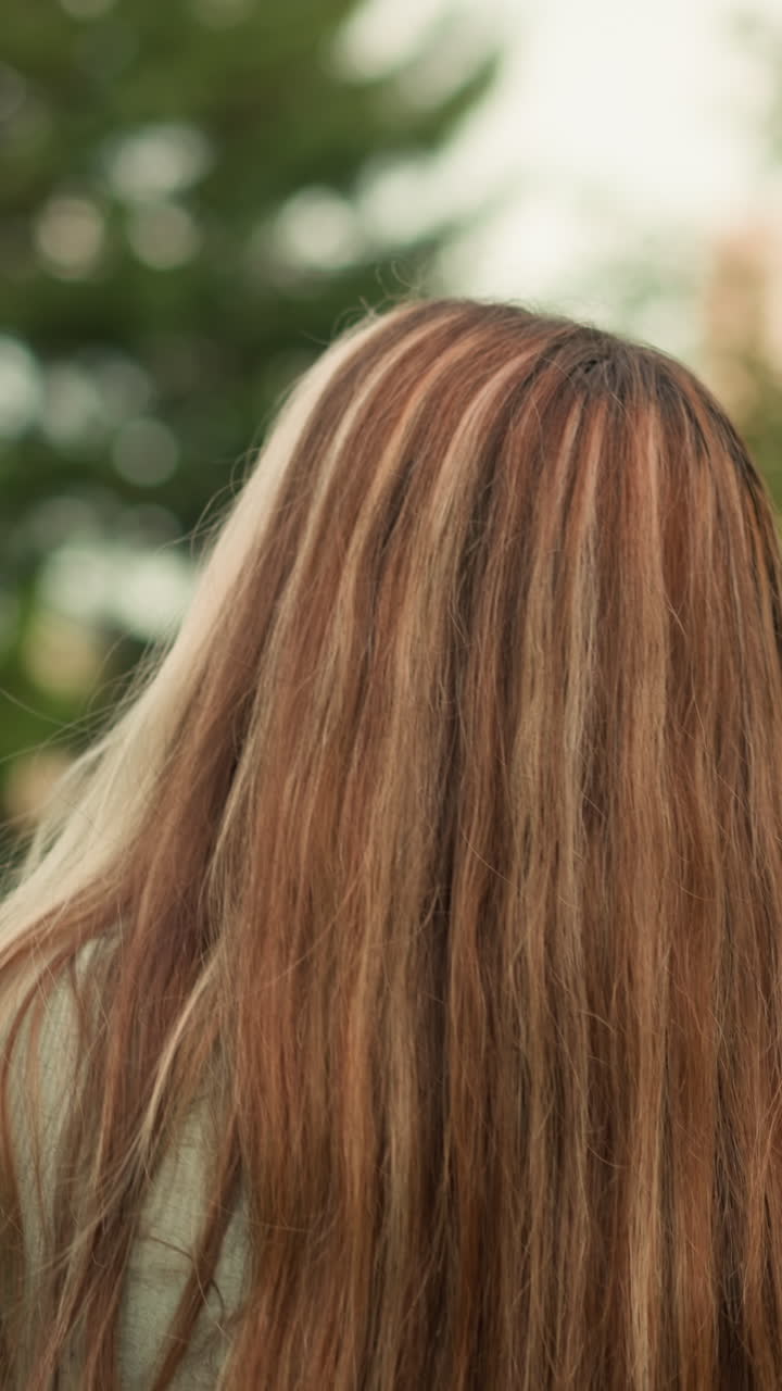 Giovane donna vista da dietro mentre percorre un sentiero con lunghi capelli biondi fluenti che le ricadono sulla schiena, circondata da una vegetazione lussureggiante. Cammina pensierosa.