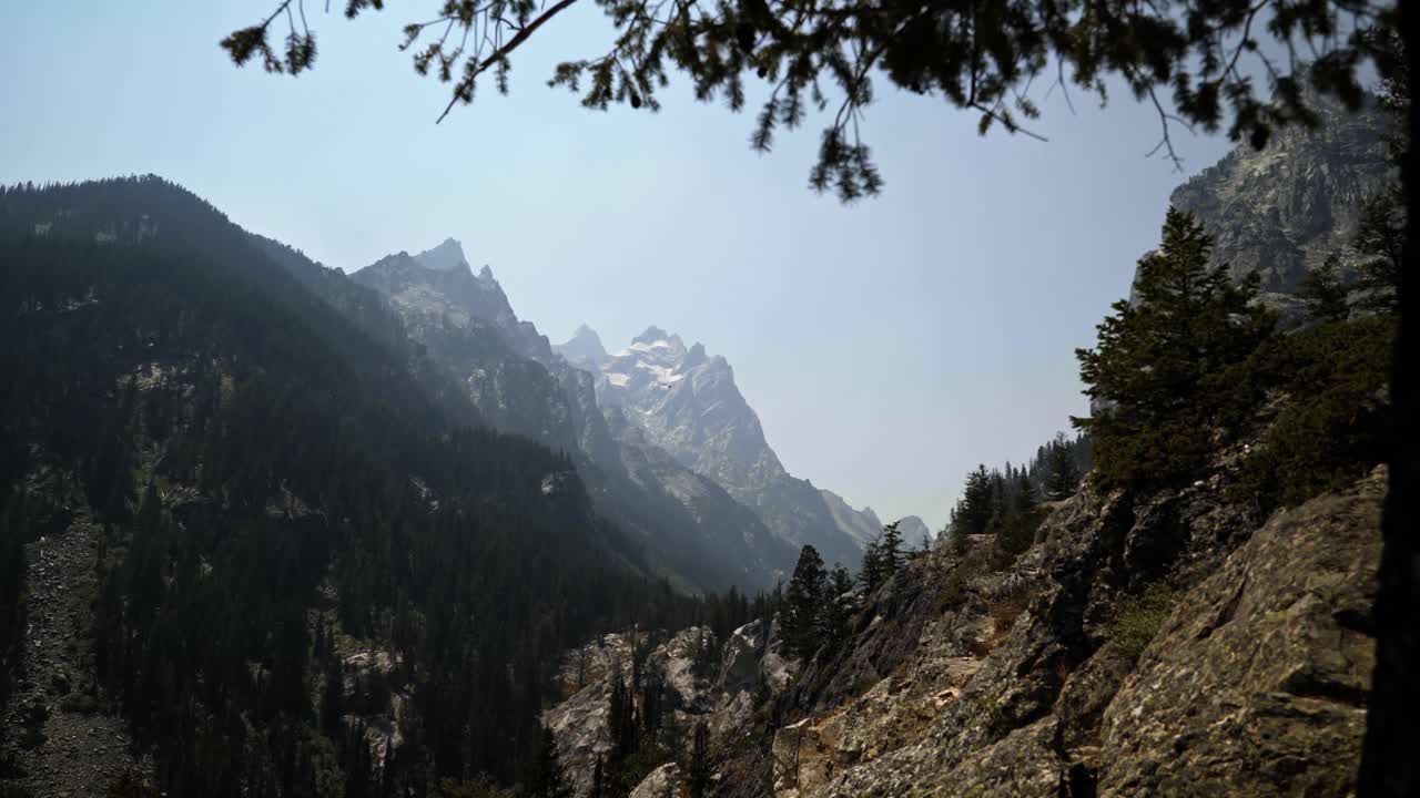 Stunning landscape nature dolly in shot of the cascade canyon valley on a hike in the Grand Teton National Park with ragged mountain peaks with glaciers on a warm hazy summer day in Wyoming, USA.