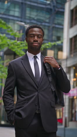 vertical video portrait of confident young businessman wearing suit standing outside offices in the financial district of the city of london uk shot in real time 1