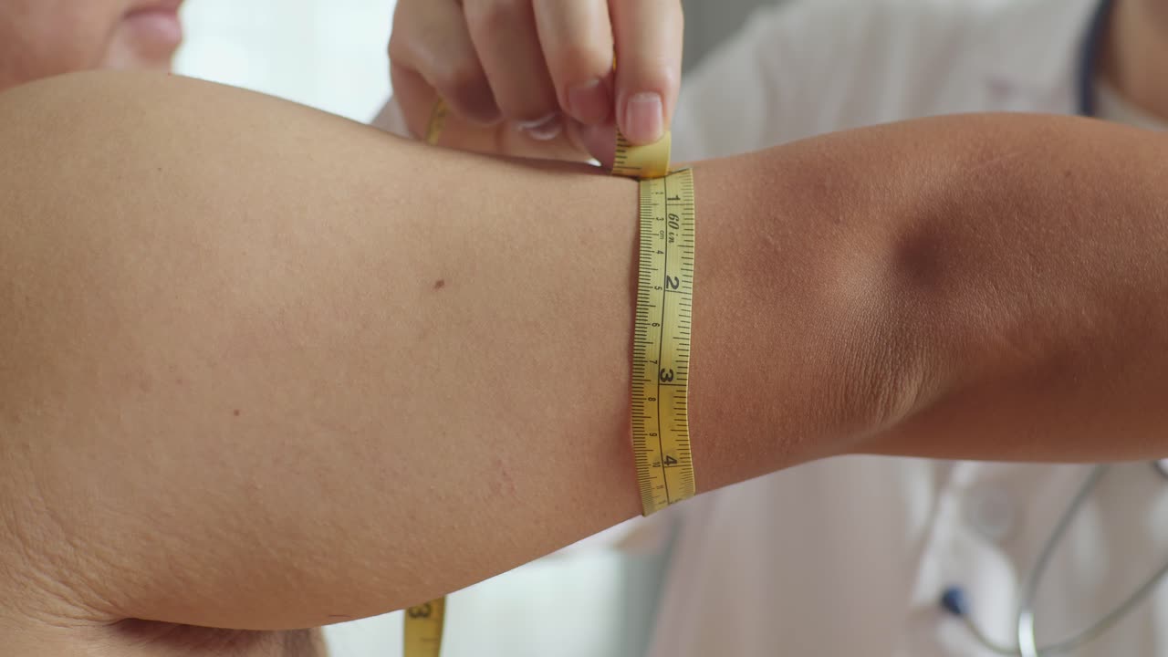 한 남성 환자의 팔을 측정하는 테이프를 사용하여 남성 의사 손의 근접