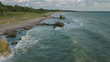 beautiful aerial establishing view of karosta concrete coast fortification ruins, sunny summer evening, golden hour light, stormy waves at baltic sea, slow motion drone shot moving forward