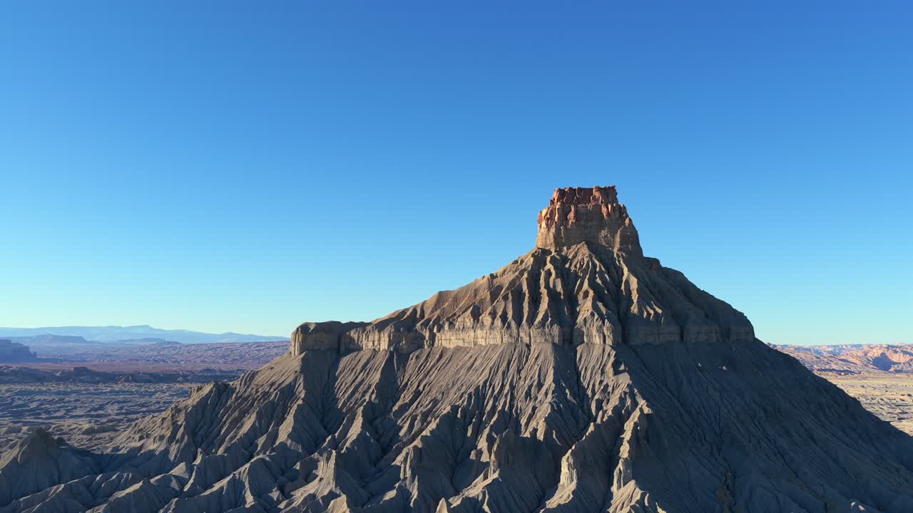Un drone cattura la topografia surreale e aliena delle badlands dello Utah. Le creste grigie e nette e le ombre profonde di Factory Butte creano un'atmosfera ultraterrena per un'avventura di viaggio nel deserto.