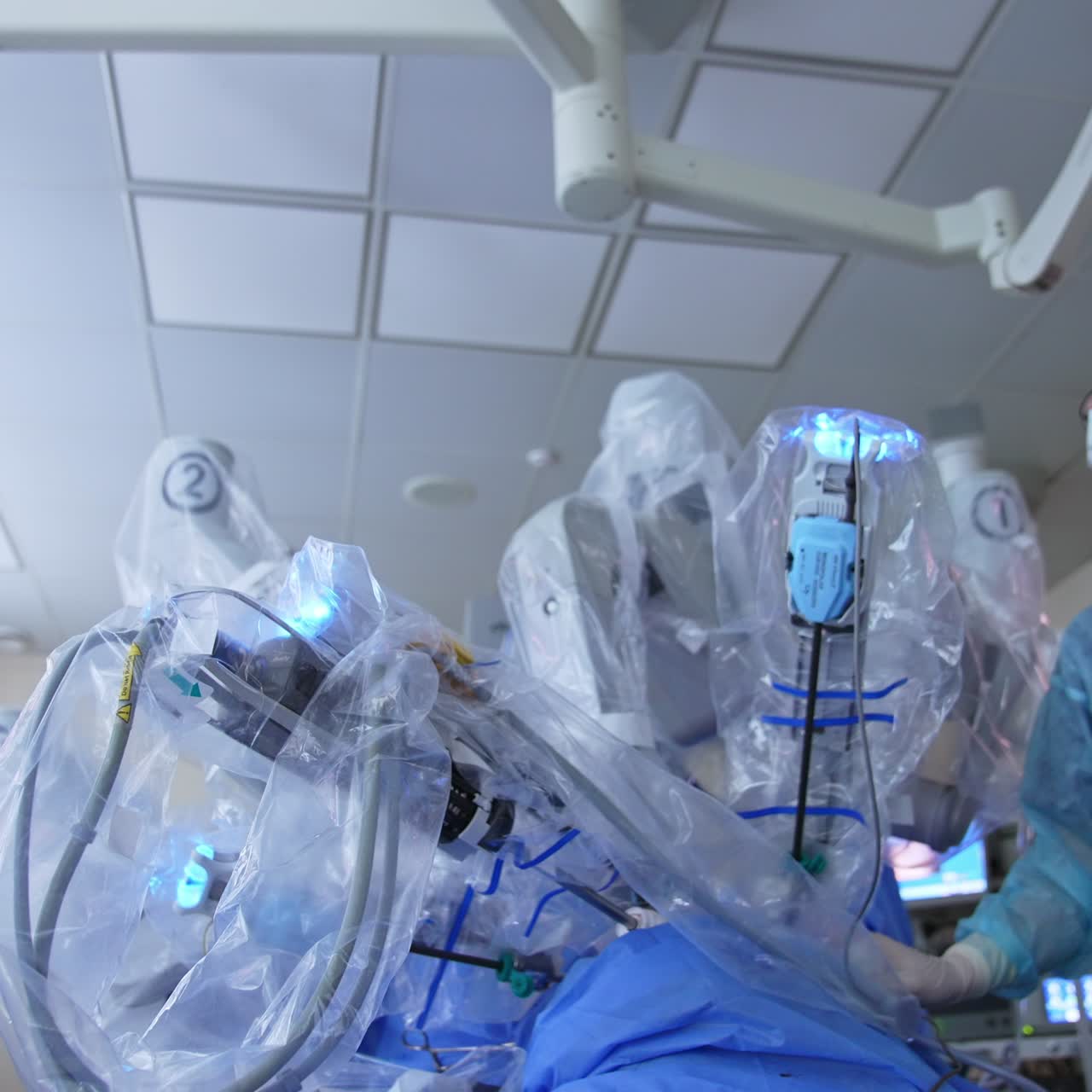 Surgeon in glasses with instrument in hand comes to a robotic equipment. Doctor watches the screen intently. Low angle view
