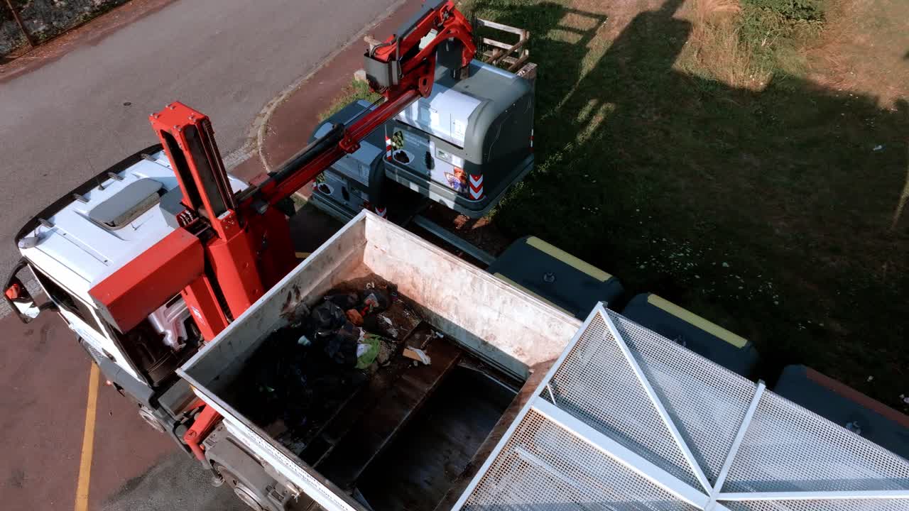 el camión de basura está recogiendo vidrio reciclado de contenedores en la carretera, levantándolos y descargándolos en la parte trasera del camión, concepto de reciclaje de vidrio