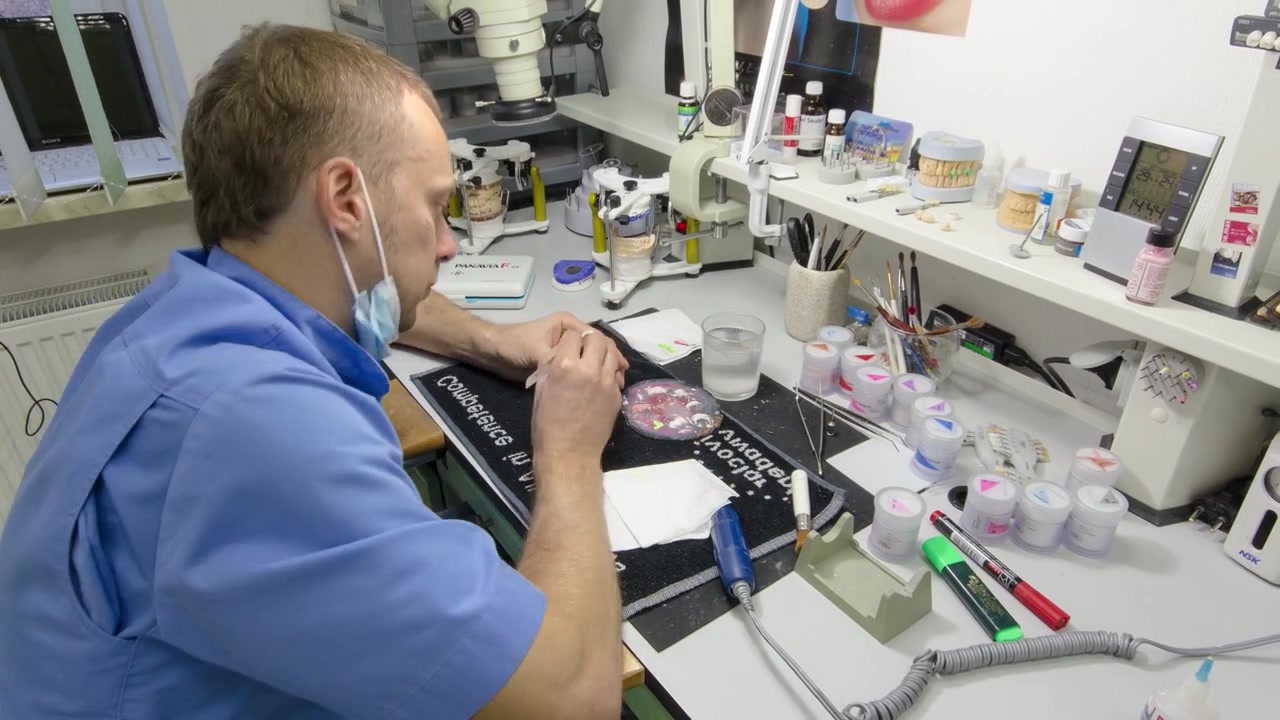 Un tecnico dentale lavora con una protesi dentale completa in metallo-ceramica inferiore e superiore, timelapse in fase finale. Il dentista lavora con un pennello su un modello di mascella in un laboratorio clinico