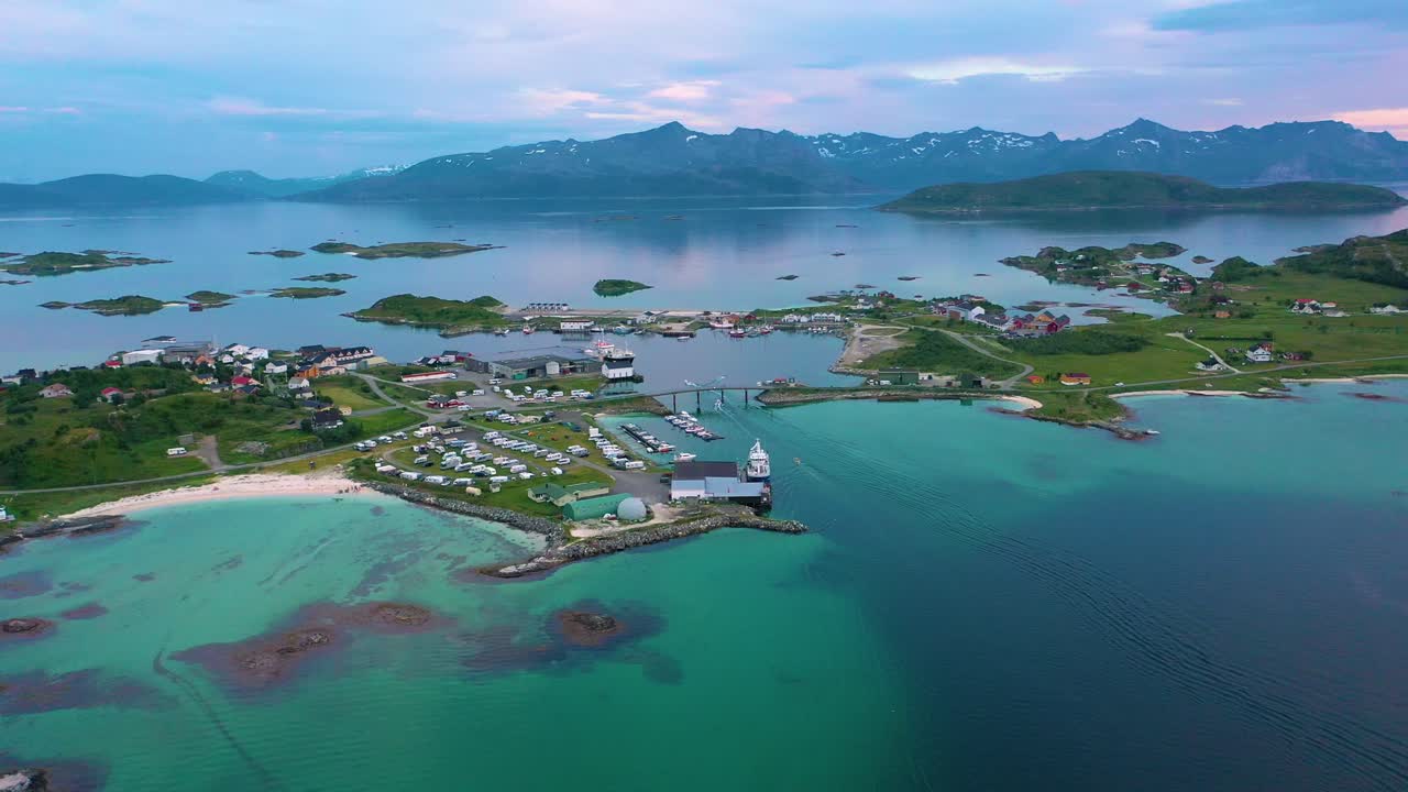Drone shot of three boats driving under a bridge, arriving at a harbor at the Sommaroy town, in turquoise arctic water of the Barents sea, summer evening, in Troms, Norway - orbit, aerial view