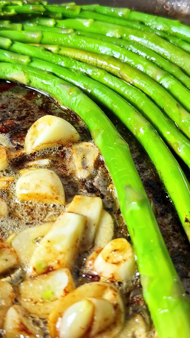 Espárragos verdes frescos y ajo chispeando en mantequilla, capturando la simplicidad de la cocina casera de temporada.