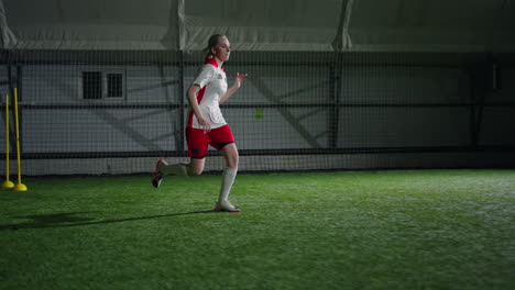 a female soccer player runs on a turf field during a training session.