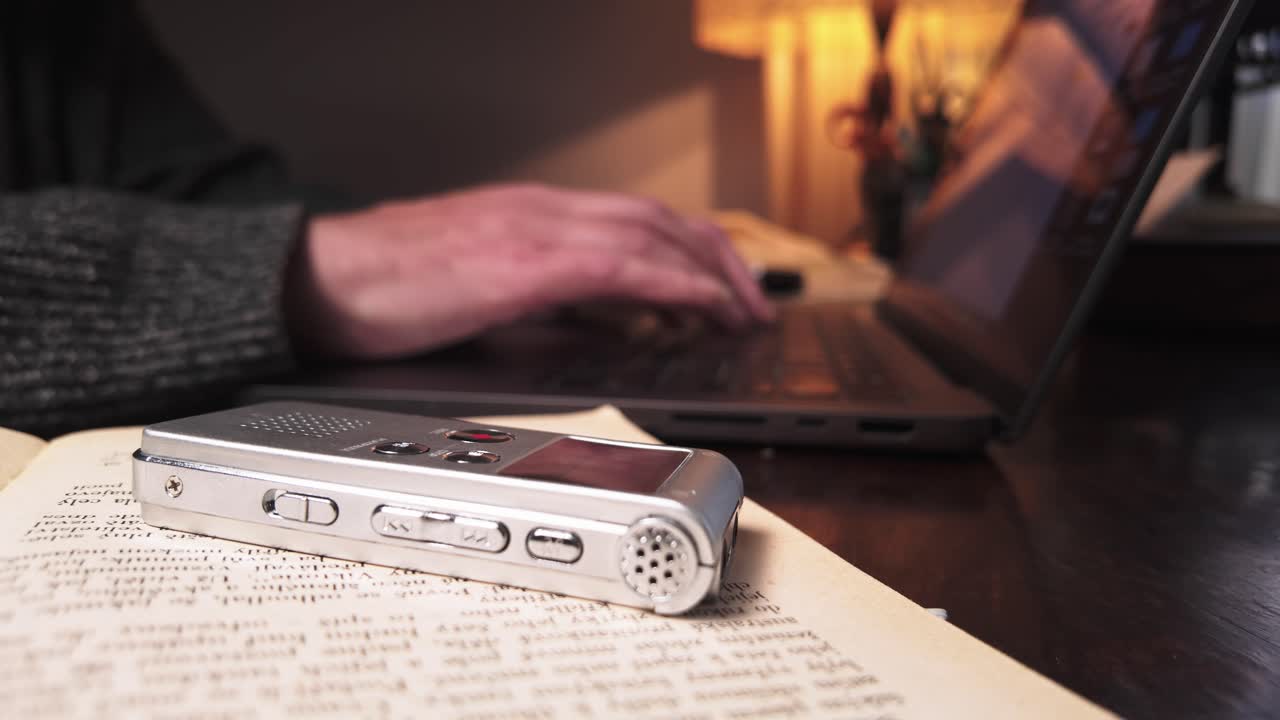 Man uses dictaphone audio recording to type up report on home laptop SIDE VIEW