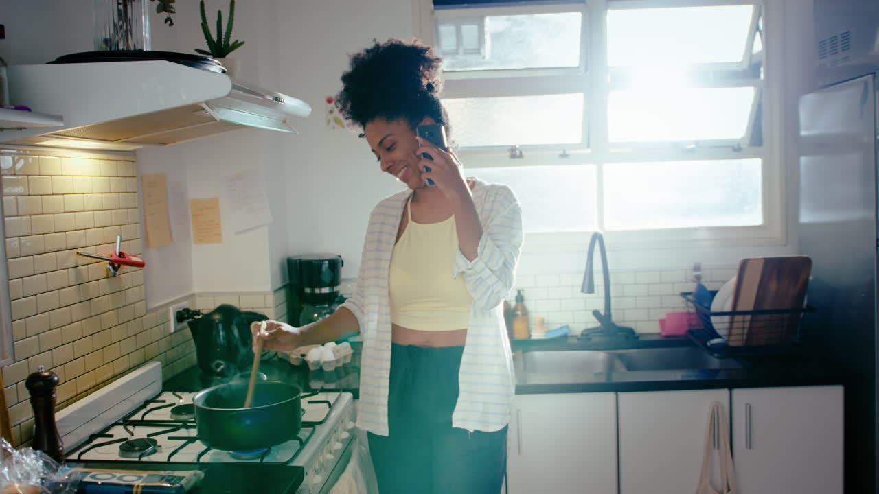 joven negra hablando por teléfono mientras cocina en la cocina