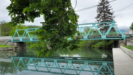 Türkise-Eisenbrücke-Mit-Gehschuss-Und-Baum-Im-Vordergrund