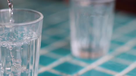 close-up sequence of liquid being poured into a clear glass on a blue checkered tabletop.
