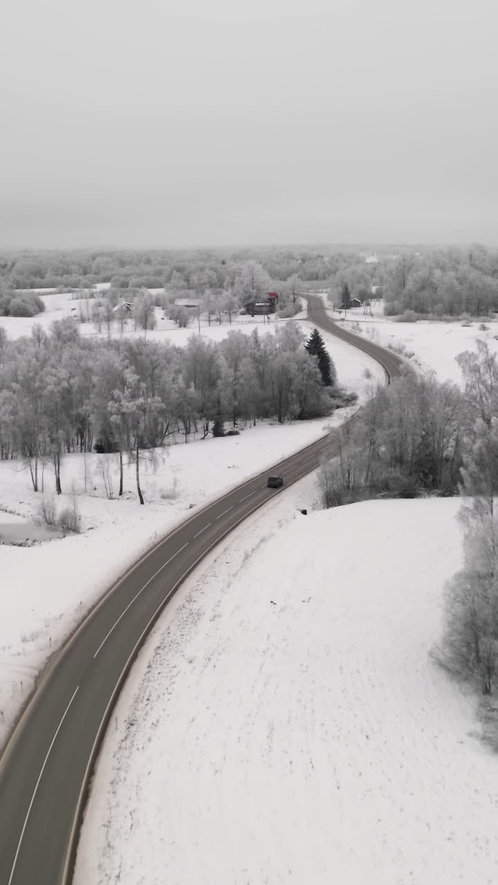 Car driving on a winding road in countryside landscape with snow covered ground and frost on the trees. Vertical aerial view with winter scenery and frozen forest.