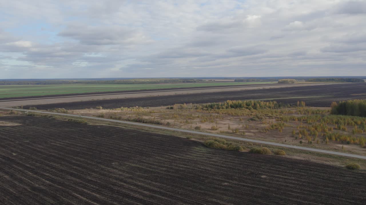 Bredt luftlandskab af dyrkede og brakmarker med en grusvej og skovkant under overskyet himmel i Ural-regionen, Rusland, roligt landskab