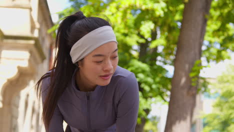 Close-Up-Of-Young-Woman-Exercising-Running-Along-City-Street-Wearing-Wireless-Earbuds-Stopping-To-Rest