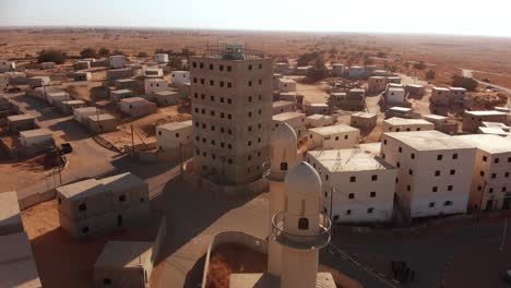 aerial shot of two mosques and big building in an old empty city in the desert in palestine near gaza while camera orbit around them at sunset.