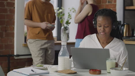 girl with headphones having breakfast and working on laptop computer in a shared flat 1