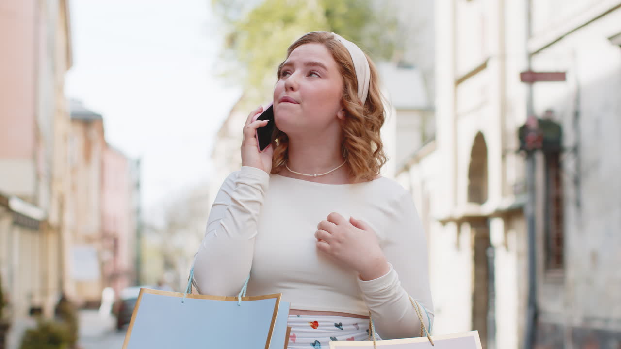 Excited woman shopaholic consumer after shopping sale with full gift bags talking on smartphone