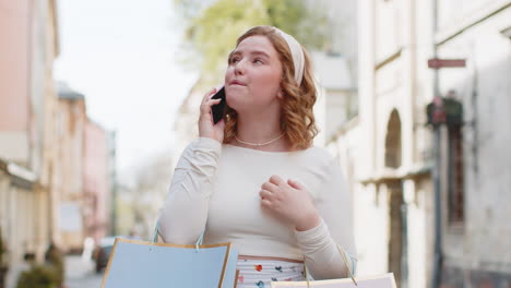 excited woman shopaholic consumer after shopping sale with full gift bags talking on smartphone