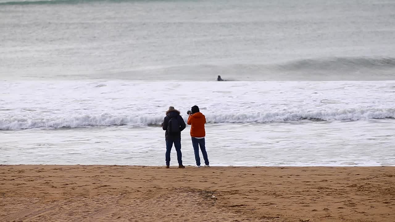 손에 카메라를 들고 해변에서 걷고 말하는 두 남자