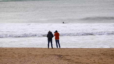 two-mens-walking-and-speaking-on-beach-with-camera-on-hands