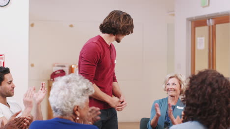 Man-Standing-To-Address-Self-Help-Therapy-Group-Meeting-In-Community-Center