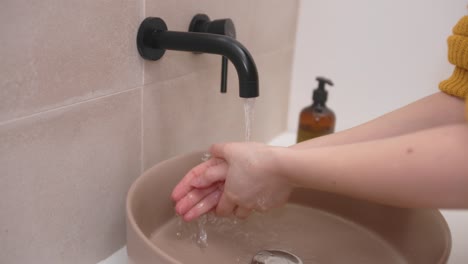 mujer enciende el grifo negro y se lava las manos en el fregadero del baño