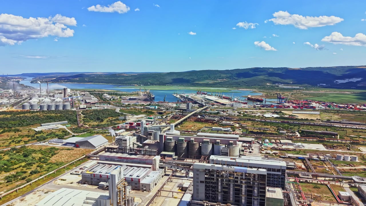 Gran zona industrial con fábricas, edificios y un río al fondo bajo un cielo azul y nubes