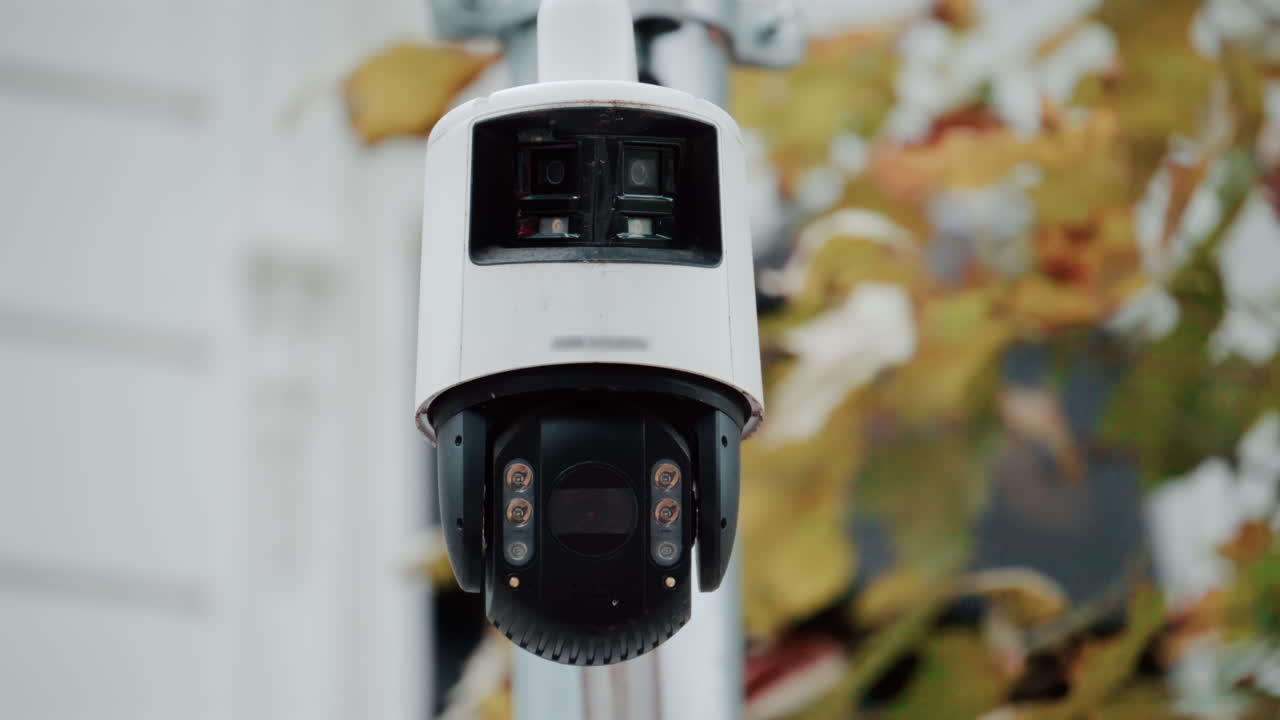 Close up of a security surveillance camera mounted on a pole with blurred autumn leaves in the background