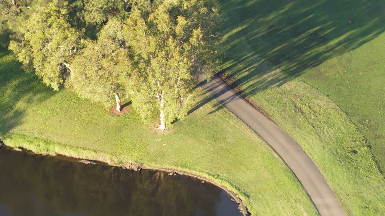 Aerial footage of a golf course with a cart on a path, surrounded by trees and water, during golden sunset hour