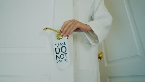 woman in bathrobe hangs do not disturb sign on doorknob of door