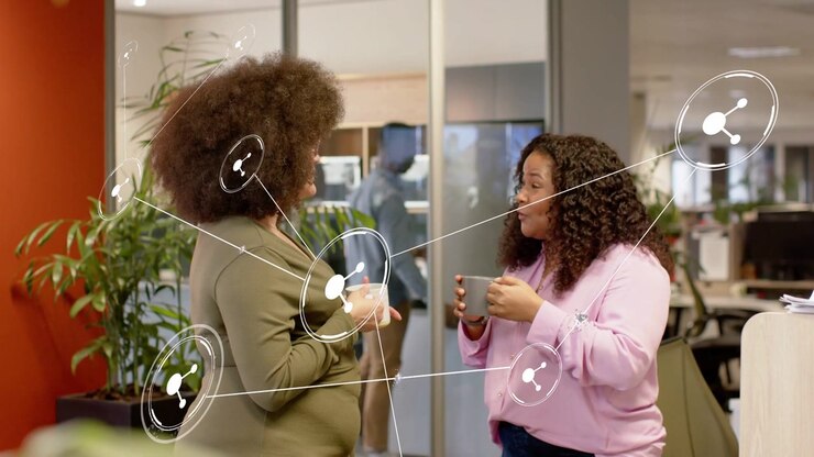 Due donne che tengono delle tazze e stanno in ufficio, conversando e avviando una sovrapposizione di rete che le collega.