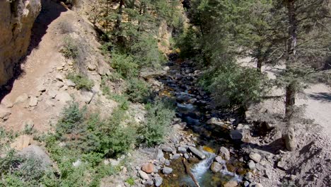 Descending-through-the-narrow-canyon-cliff-walls-to-the-shallow-creek-below---aerial-slow-motion