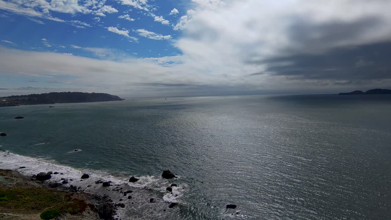 Calmo panorama marino con onde che si infrangono sugli scogli a riva e uno sfondo di cielo blu nuvoloso.