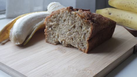zoom in view of banana bread cut in half on a wooden board with a banana in the back.