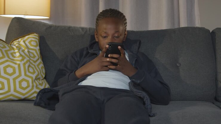 Ragazzo a casa seduto sul divano la sera mentre usa il cellulare