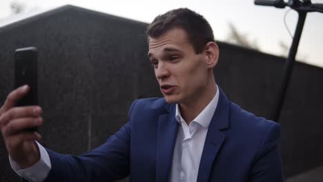 Attractive-Businessman-Sitting-On-The-Stairs-And-Does-Video-Cahtting-On-Smartphone-Outside-1