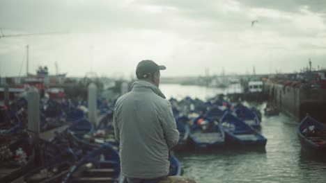 man standing and watching in front of harbor of essaouira morocco looking many blue fishing boats , authentic african sea life