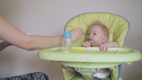 mommy feeds little son with wholesome meal in highchair