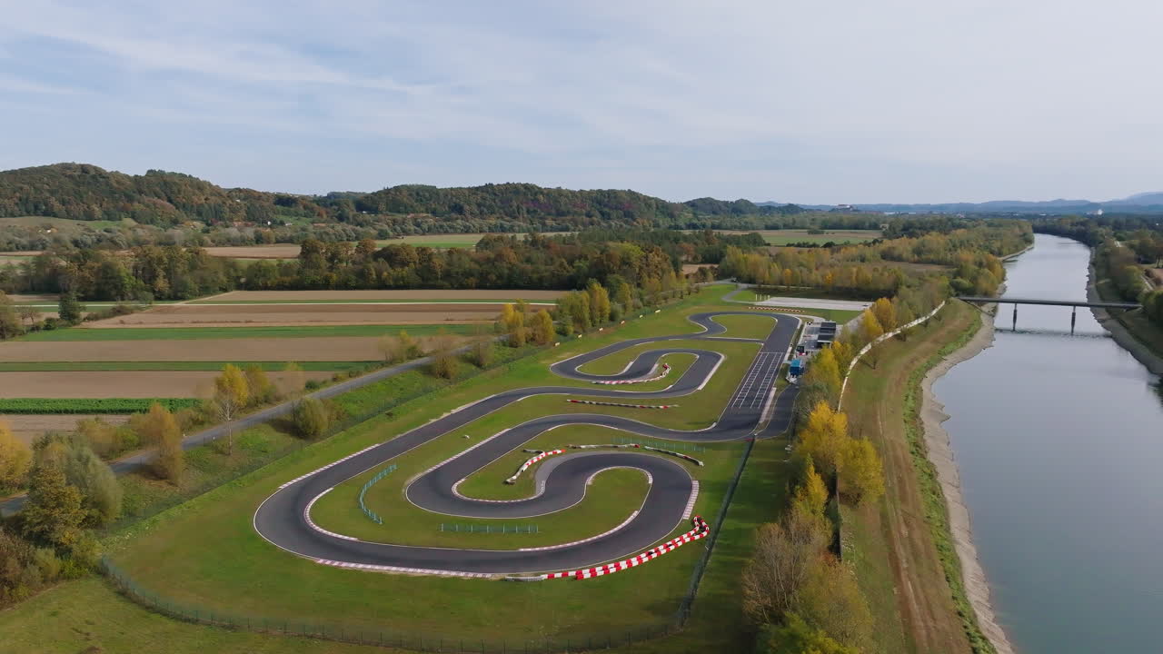 Luftfoto av racerkartbane omgitt av jorder og trær med en elv som renner langs siden