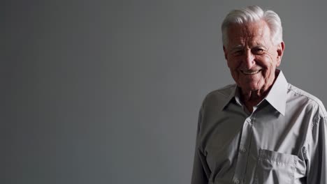 un caballero anciano sonriendo y señalando, expresando una comunicación amistosa a través del lenguaje corporal atractivo contra un telón de fondo de estudio gris uniforme