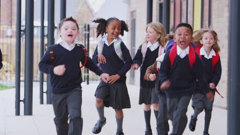 niños felices de la escuela primaria en uniformes corriendo por un pasillo fuera de su edificio escolar, vista delantera
