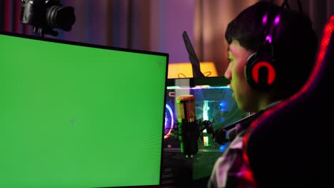 close up back view of asian boy streamer stretching after using green screen personal computer. live stream on desk illuminated by rgb led strip light