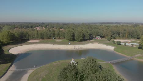 fly over of a constructed recreational lake with green grass fields and beaches revealing a bungalow park behind it in the netherlands