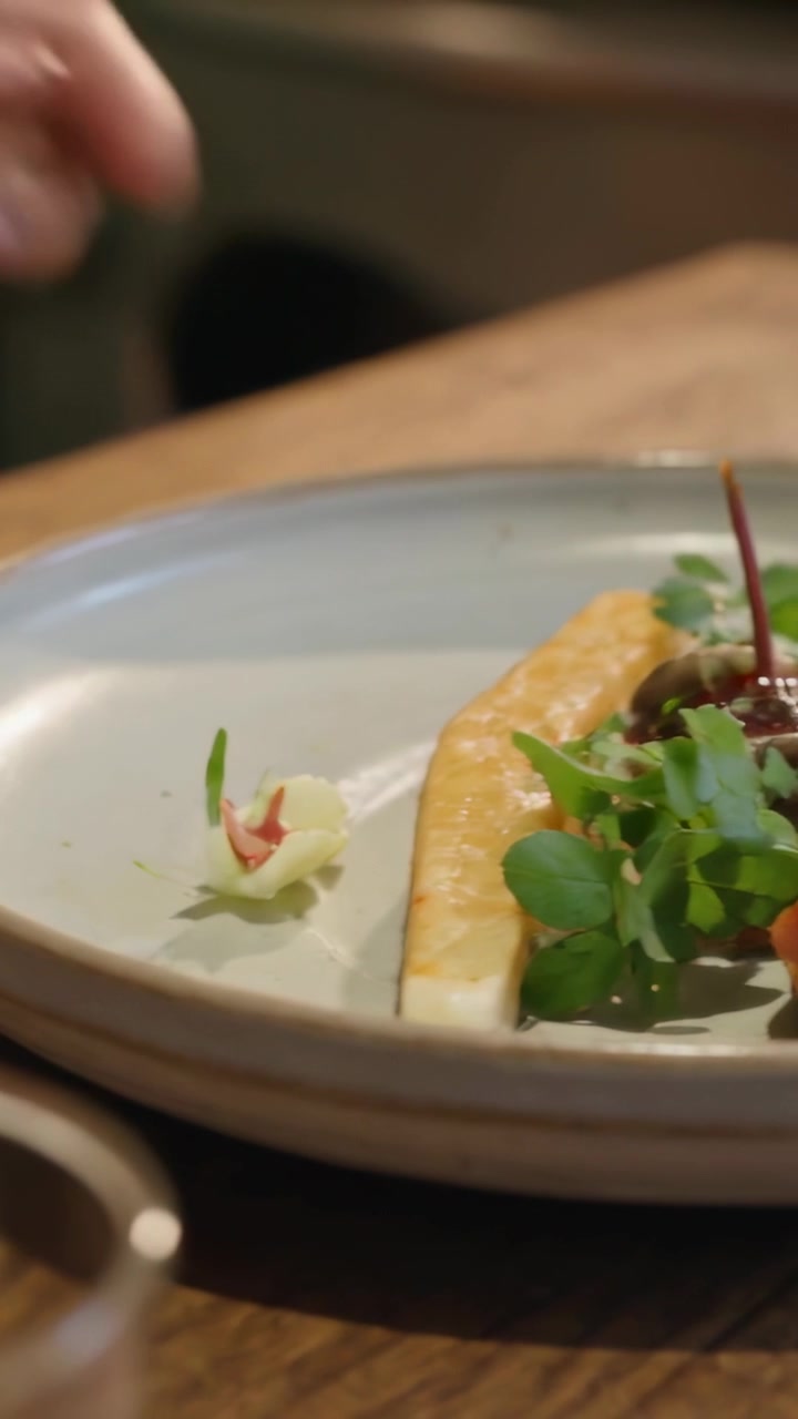 Video vertical: Manos de un chef aplicando salsa con una cuchara en un plato con pescado en el pase final.